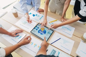 A group of hands all pointing towards data and information which is presented on a table